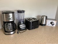 Full view of all five kitchen appliances on a countertop: Sunbeam coffee maker, Hamilton Beach blender, Proctor Silex toaster, Sunbeam kettle, and boxed Toastmaster hand mixer.