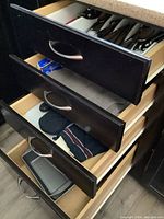 Open kitchen drawers showing utensils like cutlery and can openers in a white plastic organizer, dish towels and textile kitchen accessories, and metal bakeware trays and pans.