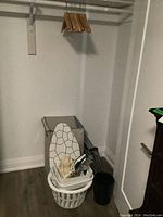 View of laundry hamper, ironing board, clothes basket, drying rack, trash can, and wood hangers on a hanging rod