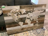 Photo of mixed media world map artwork on wooden plank background with metal map overlays and compass rose detail.