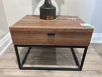 Front view showing laminate wood top and drawer front, black metal base frame, and black metal drawer pull handle