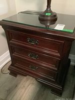 Front view showing three drawers, metal drawer pulls, and glass top with lamp and price tag on top.