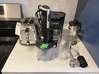 Photo showing the Oster two-slice toaster, hand blender with container and attachments, Black and Decker coffee maker, and French press on kitchen countertop.
