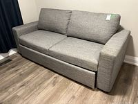Gray fabric pull-out sofa bed in living space, showing the sofa in closed position with removable back cushions.