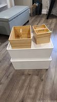 Wooden storage boxes stacked on top of two white plastic storage totes on a wood floor.