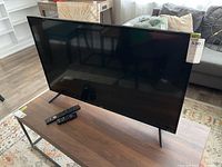 Front view of the 43-inch RCA Roku TV on a wooden table with two remote controls placed in front.