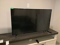 Front view of the black Vizio 43-inch TV on stand legs, remote next to it on the right side.