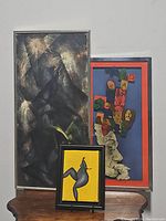 Three framed abstract art pieces displayed together on wooden surface against wall.