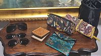 View of all sunglasses, wallets, pouches, and bags included in the lot, placed on a wooden surface with a gold framed mirror in the background