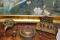 Photo showing all four brass collectible items on wooden surface: ornate double inkwell, enameled trinket container, brass trivet, small tumbler/mortar, pestle.