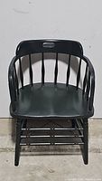 Front view of the black captain spindle back chair showing the curved backrest with vertical spindles and armrests.