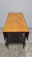 Front view of the farmhouse style drop leaf wooden table with drop leaves folded down, showing natural wood grain and simple structure.