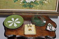 All six items displayed on wood table under framed floral artwork: avocado green lotus plate, clear glass plates, HB Quimper basket dish, Denmark pottery tray, salt and pepper shakers.