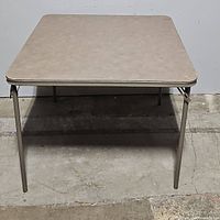 Front view of folding card table showing beige vinyl surface and metal legs