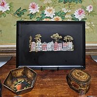 Photo featuring all three items on wooden table: black serving tray with painted houses and trees, hexagonal fruit motif dish, and floral trinket box