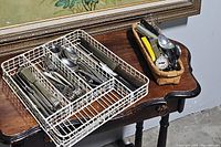 White wire flatware tray with assorted metal cutlery (forks, spoons, knives) on a wooden table