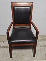 Front view of dining chair showing mahogany wood frame and black leather seat and backrest.