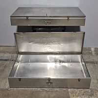 Full view of one metal storage container open showing embossed floral design inside lid and latch locks.