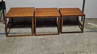 Front view of three teak nesting tables arranged side by side.