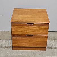 Front view of the oak nightstand with two closed drawers, showing natural wood grain and finger groove handles.