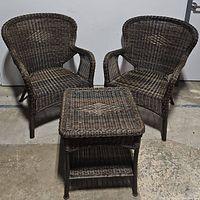 Front view of two brown rattan wicker patio chairs with square end table between them showing woven design and overall structure.
