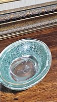 Speckled blue-green glass bowl with textured surface placed on wooden table.