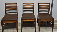 Front view of the set of three teak dining chairs with brown geometric fabric seats in used condition.