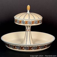 Two-tiered lidded serving dish with floral border and finial top, shown against black background