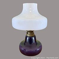 Front view of the 1960s Danish oil lamp showing the purple Holmegaard glass base, brass burner, and white opaque glass shade.