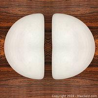 Top view of the two half moon shaped opaque white glass sconces placed on a wood surface showing their symmetrical shape.