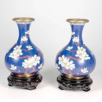 Front view of a pair of blue cloisonne vases with white floral and bluebird enamel decoration seated on carved wooden stands.