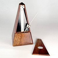 Front view showing the wooden metronome with the removable cover set aside revealing the white tempo scale and metal pendulum arm.