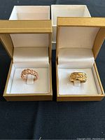 Two rings in gold-tone boxes side by side on black background