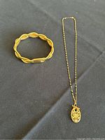 Braided bracelet and toggle chain necklace with filigree pendant laid flat on black surface