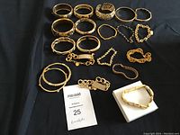 Full overview of all 15 bracelets laid out on a black surface showing various gold-toned designs and shapes.