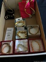 Photo of seven different bracelets placed in open boxes and black jewelry tray inside a cardboard box, two pink satin jewelry cases on the side