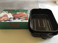 Nature's Oven Clay Baker in original box next to two large black speckled roasting pans
