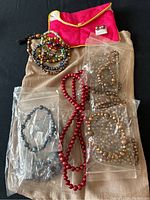 All pearl jewelry sets including bronze, periwinkle, red freshwater pearl strands with bracelets and 14K gold bronze pearl earrings displayed on fabric background with fabric bags.