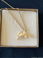 Photo of the yellow gold rope chain with white dolphin pendant set on cream fabric in a box.