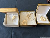 Photo showing three dolphin pendants and a gold-tone chain with spring ring clasp inside jewelry boxes on a table.