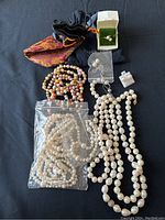 Overview of all items on black background including necklaces, strand in plastic bag, bracelets, earrings, ring and pouches