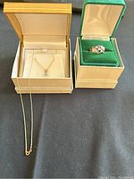Wide view showing ring in green box and pendant with chain in beige box