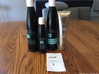 Four hair care and hand cream products on wooden table including shampoo, conditioner, serum and hand cream tube.