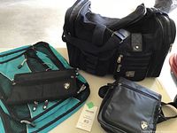 Photo showing the black HEYS duffle bag next to two turquoise packing cubes and a black hanging travel jewelry case all arranged on a surface.