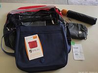 Full set of 5 packing cubes (3 red, 2 navy blue) stacked, with navy blue Hi Lite Crossbody Bag, small black zippered case, and Centro black compact umbrella shown on a flat surface.