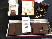 Full lot displayed including men's Rumours watch in black box, new Tilley brown leather wallet in white box, vintage Artistic cufflinks in red and white box, General Electric tie pin in brown box, and Artistic key chain in brown box.