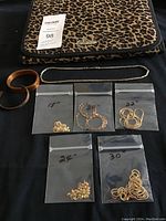 Overview of leopard-print travel case, two copper bracelets, one sterling silver chain necklace and five sealed bags of gold plated sterling silver necklaces