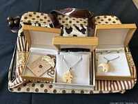 Three jewellery boxes open displaying white wildlife pendants on silver chains and a fabric jewellery travel bag beneath.