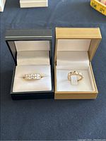 Two rings side by side in presentation boxes (black and gold)