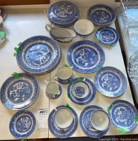 Full layout of Blue Willow dish set including larger plates, smaller plates, teacups with saucers, creamer, sugar bowl, gravy boat, and covered serving dish